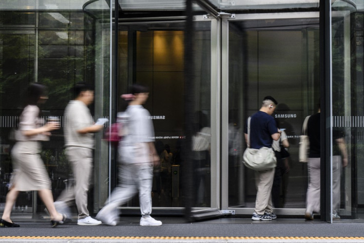 People walk past the Samsung logo displayed on a glass revolving door at the company's Seocho building in Seoul on July 31, 2024.