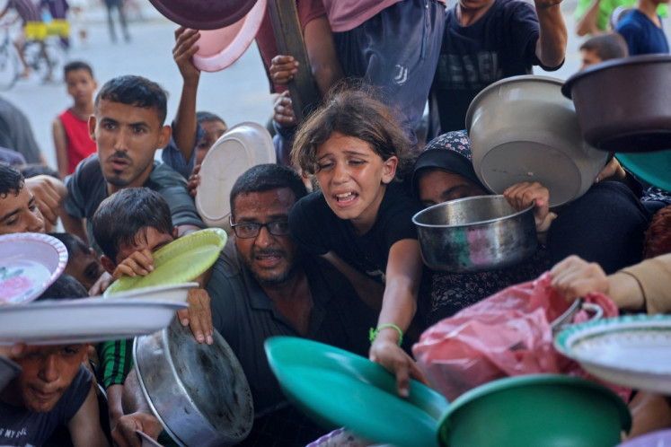 Displaced Palestinians wait to receive for food at a food distribution point, set up by young men from the Madhoun family in Beit Lahia, in the northern Gaza Strip on July 18, 2024, amid the ongoing conflict between Israel and the Palestinian Hamas militant group. UN rights experts on July 9 accused Israel of carrying out a “targeted starvation campaign“ that has resulted in the deaths of children in Gaza. The UN has not officially declared a famine in the Gaza Strip.