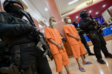 Armed officers from the National Narcotics Agency guard two suspects during a press conference on the uncovering of an international network that smuggled marijuana to Britain from Thailand and via Indonesia, in Jakarta on August 5, 2024. 