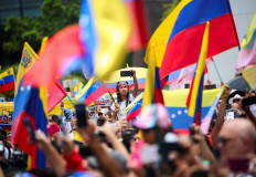 A girl uses a mobile phone as Venezuelans living in Colombia wave Venezuela's national flags during a protest against election results, in Medellin, Colombia on Aug. 7, 2024.