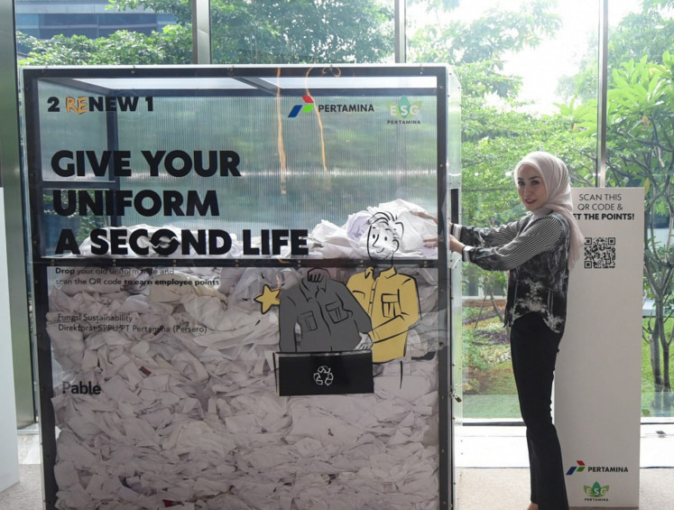 An employee places an old uniform into a bin provided by Pertamina for its sustainability program, which recycles uniforms into eco-friendly clothing and encourages all Pertamina employees to become sustainability agents to contribute to achieving Indonesia's net-zero goals.