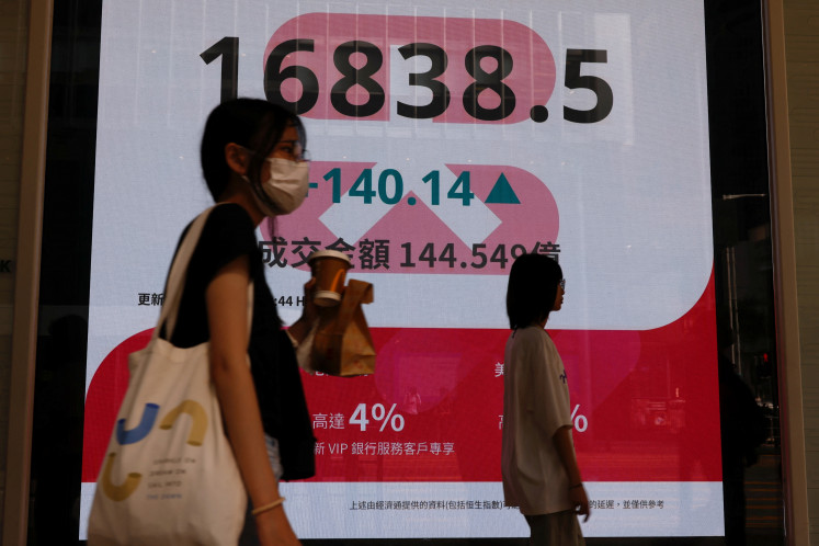 People walk past a panel displaying figures of China stock indexes and Hang Seng Index at the Financial Central district in Hong Kong, China, on Aug. 6, 2024.