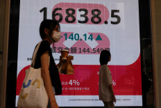 People walk past a panel displaying figures of China stock indexes and Hang Seng Index at the Financial Central district in Hong Kong, China, on Aug. 6, 2024.