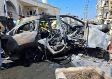 Civil defence members stand near a burnt car after an Israeli strike on the outskirts of the southern port city of Sidon, according to two Palestinian sources, in Lebanon on August 21, 2024. 