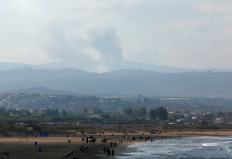 A view shows smoke on the Lebanese side of the border with Israel, as people walk along a beach in Tyre, amid ongoing cross-border hostilities between Hezbollah and Israeli forces, southern Lebanon August 25, 2024. 