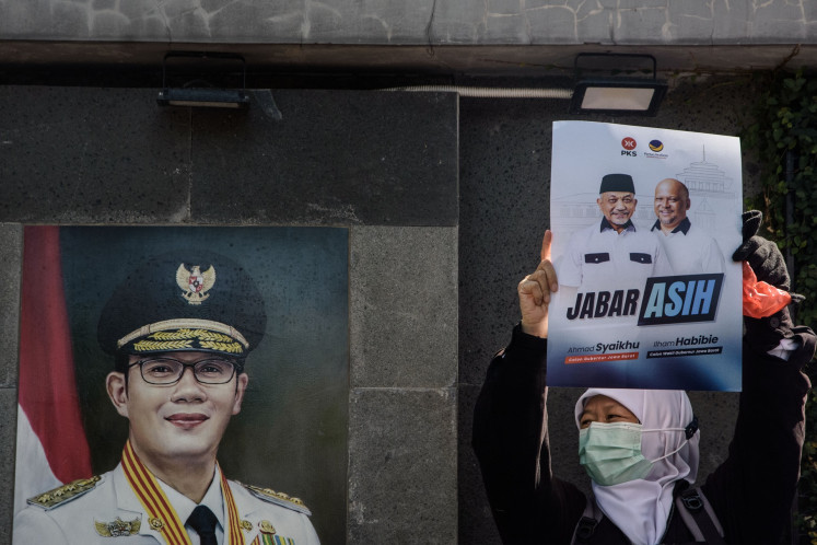 A supporter holds up a poster of a West Java gubernatorial ticket Ahmad Syaikhu and Ilham Habibie next to a portrait of former West Java governor Ridwan Kamil in Bandung, West Java on Aug. 29, 2024. Despite his popularity in West Java, Ridwan is running for governor in Jakarta. 