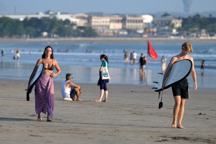 Foreign tourists carry their surfboards on Aug. 3, 2024, as they walk along Kuta beach near Denpasar, Bali.