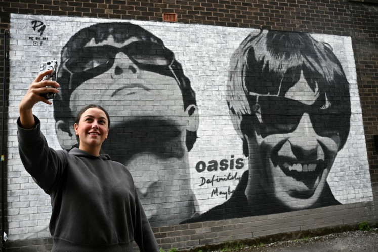 Fan Emily McShane, takes a photograph of a new street artwork depicting Oasis' Liam and Noel Gallagher, created by Manchester-based street artist Pic.One.Art. on the side of the Sifters Record store in Burnage, a suburb of Manchester, northern England on Aug. 27, 2024. British rock legends Oasis announced Tuesday they will reunite for a worldwide tour, as brothers Liam and Noel Gallagher ended an infamous 15-year feud. The band behind hit songs including “Wonderwall“, “Don't Look Back In Anger“ and “Champagne Supernova“, will play an initial 14 gigs next year in Cardiff, Manchester, London, Edinburgh and the Irish capital, Dublin, starting in July.