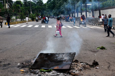 A pedestrian crosses a road near smoking objects during a protest demanding the stepping down of Bangladeshi Prime Minister Sheikh Hasina following quota reform protests by students in Dhaka, Bangladesh on Aug. 4, 2024.