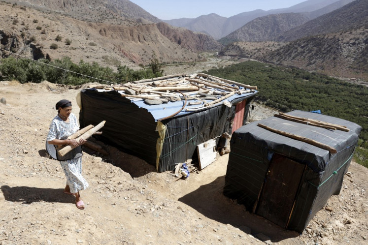 A woman carries wood as she walks in front of temporary housing structures in Douar Tiniskt, in the el-Haouz province in the High Atlas Mountains south of Marrakesh, on Aug. 27, 2024, almost a year after a devastating 6.8-magnitude earthquake struck the country. The 6.8-magnitude quake killed almost 3,000 people and damaged the homes of over two million people across the High Atlas region.