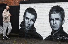 A pedestrian walks past a mural created by artist Scott Wilcock aka Snow Graffiti, depicting Liam Gallagher (left) and Noel Gallagher (right) members of the British rock band Oasis, and painted outside the pub Whitefield, near Heaton Park, in Manchester, northern England, on September 2, 2024. 
