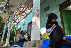 Students attend to their assignments on Aug. 22, 2024 on the porch of MIS Al-Khaeriyah elementary school in Tangerang regency, Banten. The private Islamic school, which is heavily damaged, has resumed learning activities in outdoor spaces and residential homes for safety.
