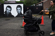 A woman pushes a buggy as she walks past a mural created by artist Scott Wilcock aka Snow Graffiti, depicting Liam Gallagher (left) and Noel Gallagher (right) members of the British rock band Oasis, and painted outside the pub Whitefield near Heaton Park in Manchester, northern England, on Sept. 2, 2024. Oasis, which was integral to the 1990s Britpop scene but split in 2009, announced on Aug. 27 it will reunite next year for a worldwide tour, starting with 17 concerts in the UK and Ireland. The band are set to play five of their concerts at Manchester's Heaton Park, one of Europe's largest urban open spaces.