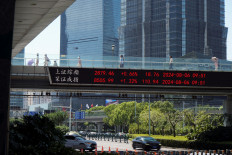People walk on an overpass with a display of stock information in front of buildings in the Lujiazui financial district in Shanghai, China, on Aug. 6, 2024.