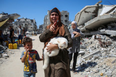 A Palestinian woman holds a cat as she walks pas the rubble of houses destroyed in the Israel's military offensive, amid the Israel-Hamas conflict, in Khan Younis, in the southern Gaza Strip, September 26, 2024. 