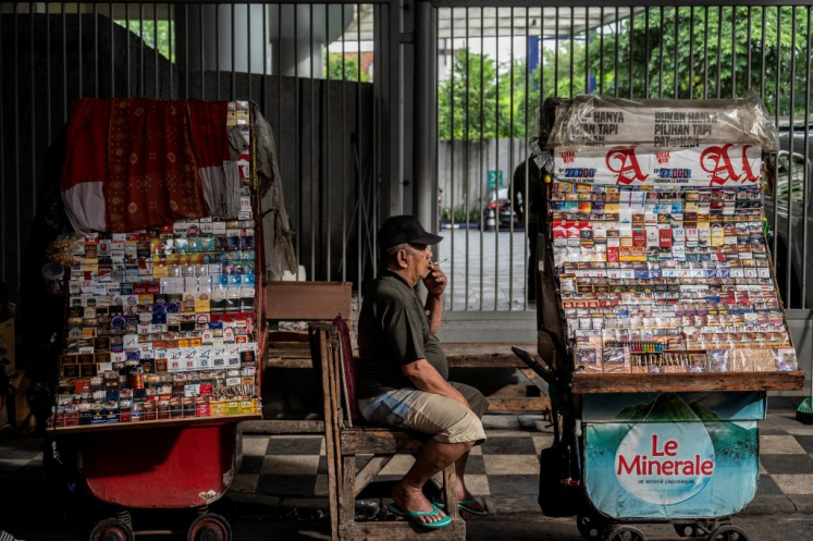 A cigarette vendor smokes on Jan. 29, 2023, as he awaits customers at his roadside stall in Surabaya, East Java.