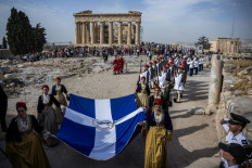 Women in traditional Greece attire hold the edges of a large Greek flag on the top of the Acropolis hill during a ceremony to mark the 80th anniversary of the liberation of Athens from Nazi occupation in Athens, Greece on Oct. 12, 2024.