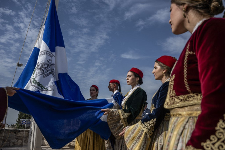 Wanita berpakaian tradisional bersiap mengibarkan bendera nasional Yunani di puncak bukit Acropolis dalam upacara peringatan 80 tahun pembebasan Athena dari pendudukan Nazi, di Athena, Yunani pada 12 Oktober 2024.