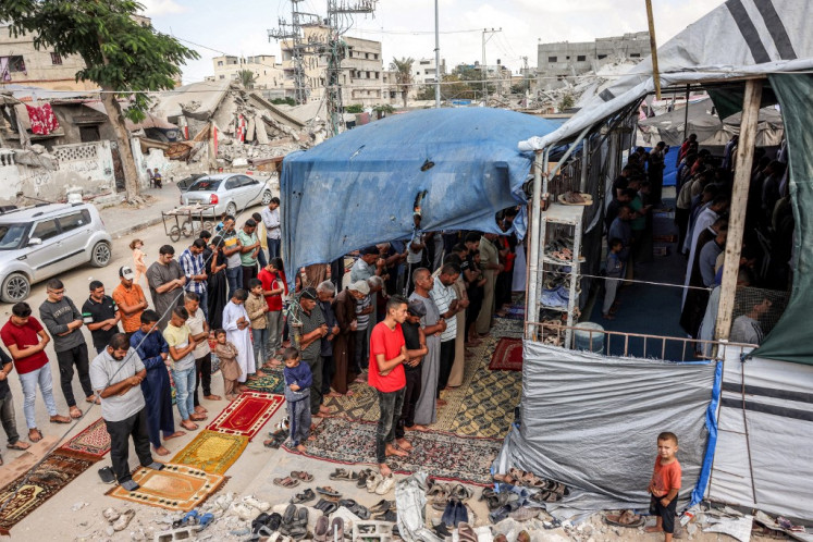 Umat ​​​​Muslim melaksanakan salat Jumat mingguan di tenda yang dikelilingi bangunan yang hancur di Khan Yunis di Jalur Gaza selatan pada 18 Oktober 2024 di tengah perang yang sedang berlangsung di wilayah Palestina antara Israel dan Hamas.