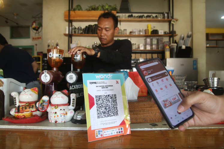 A barista prepares a beverage on Sept. 19, 2024, as a customer uses a smartphone to scan a Quick Response Indonesia Standard (QRIS) code to make a digital payment at SK Coffee Lab, a café in Kediri, East Java. 