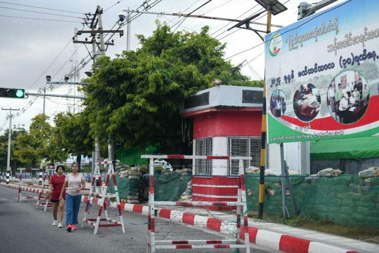 Para perempuan berjalan melewati barikade keamanan di sebuah jalan di Mandalay pada 24 Oktober 2024. Di pinggiran Mandalay, tentara Myanmar yang gugup menjaga pos pemeriksaan hanya beberapa kilometer dari pemberontak yang mengincar bekas ibu kota kerajaan berpenduduk 1,5 juta orang itu.