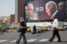 Iranians walk next to an anti-U.S. and Israeli billboard with pictures of Iranian President Masoud Pezeshkian and Iranian Armed Forces Chief of Staff, Major General Mohammad Bagheri and U.S. President Joe Biden and Israel's Prime Minister Benjamin Netanyahu, on a street in Tehran, Iran, October 27, 2024. 