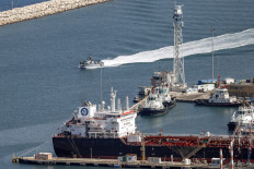 An Israeli Navy fast patrol boat cruises past tugboats and the Malta-flagged oil tanker Chrysopigi moored in the port of Haifa in northern Israel on Oct. 14, 2024.