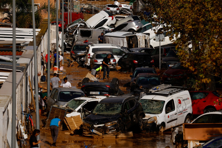 Orang-orang membersihkan jalan yang tertutup lumpur di samping tumpukan mobil setelah hujan lebat di Alfafar, Valencia, Spanyol, pada 1 November 2024.