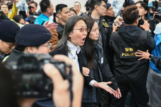 Police detain a woman (center) outside the West Kowloon Magistrates' Court in Hong Kong on November 19, 2024. Hong Kong's largest national security trial will draw to a close on November 19, with dozens of the city's most prominent democracy campaigners set to be sentenced for subversion, a charge which can carry up to life imprisonment. 
