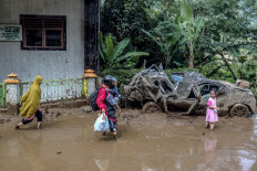 A family wades through mud, past a crushed car following landslides at the Semangat Gunung village in Karo, North Sumatra on November 25, 2024. 