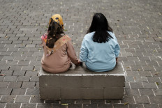 Two women whose husbands are being forced to work as scammers in Myanmar sit on a concrete bench on Oct. 16, 2024, during an interview with AFP in Jakarta.