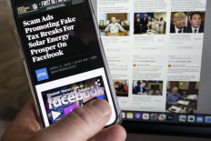 A phone screen taken on Feb. 6, 2023 displays a story about scam ads promoting fake tax breaks for solar in front of a screen showing some of the Facebook archived fake ads luring people into the scam. AFP's fact checkers have recently uncovered a slew of energy-related scams that have proliferated on Facebook, from fake incentives for solar panels in the United States to hoax electric bike giveaways in Indonesia and the sale of dud “power saving“ devices in the Philippines.