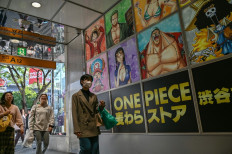People walk past advertising on April 19, 2024 for the Japanese manga series “One Piece“ at the entrance to a building in the Shibuya area of central Tokyo.