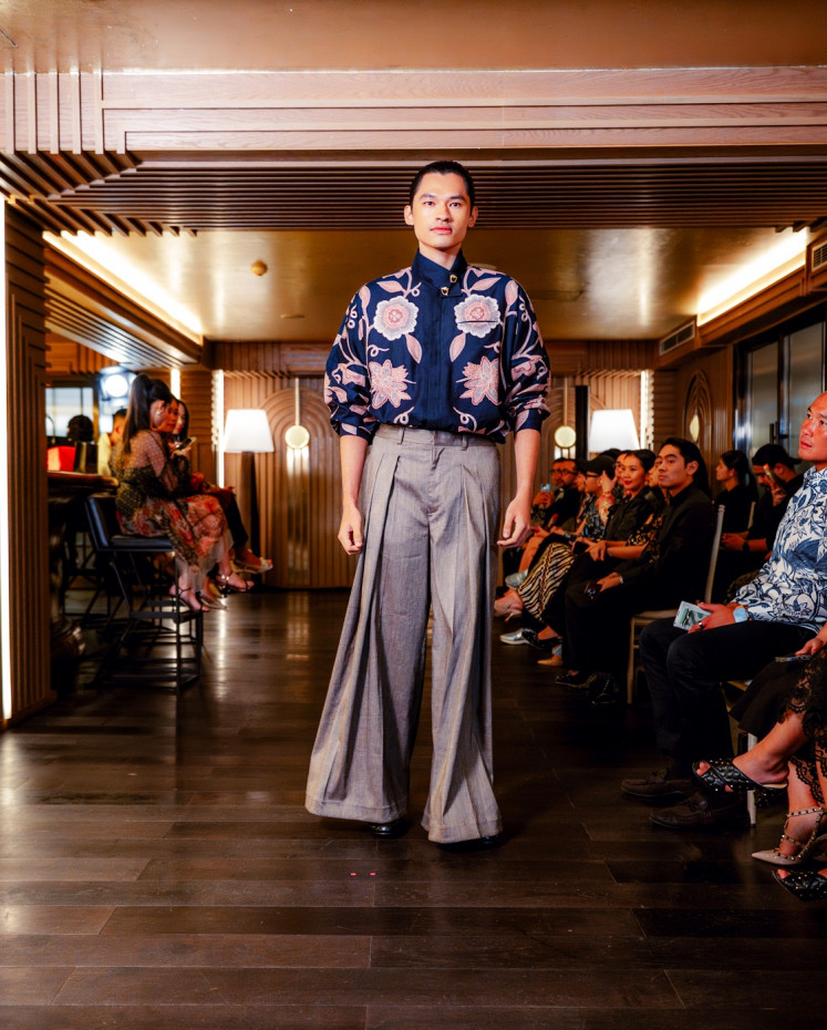 A model presents a stunning batik shirt by Iwan Tirta Private Collection, adorned with floral motifs. At a closer look, micro-patterns intricately fill the larger designs, adding depth and vitality to the batik.