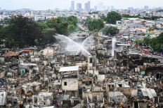 Jets of water arch over the burned-out husks of hundreds of houses on Jan. 21, 2025, as firefighters work to completely extinguish a blaze that razed through Kebon Kosong, a densely populated settlement in Kemayoran, Central Jakarta.