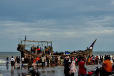 People gather around a boat carrying newly-arrived Rohingya refugees after authorities prevented the refugees from disembarking and ordered them to remain on board the vessel on Jan. 29 at Leuge Beach in East Aceh regency, Aceh. At least 75 Rohingya refugees arrived by boat at a beach in Aceh on Jan. 29, but were stopped by authorities from disembarking, according to local officials.