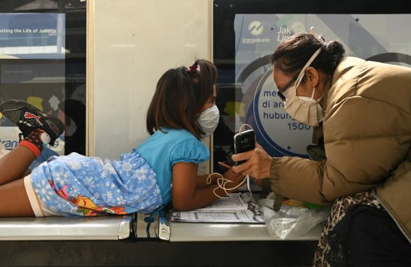 Digital childhood: A woman holds up a smartphone at a bus shelter in Jakarta for her daughter to attend a virtual kindergarten class on Aug. 31, 2021, during the COVID-19 pandemic.