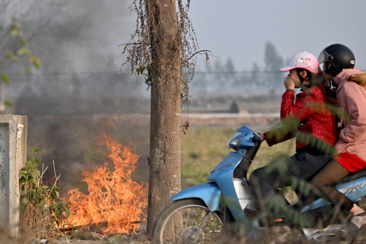 A woman covers her face as she rides a motorbike past a burning garbage dump on the side of the road in Hanoi on Jan. 20, 2025.