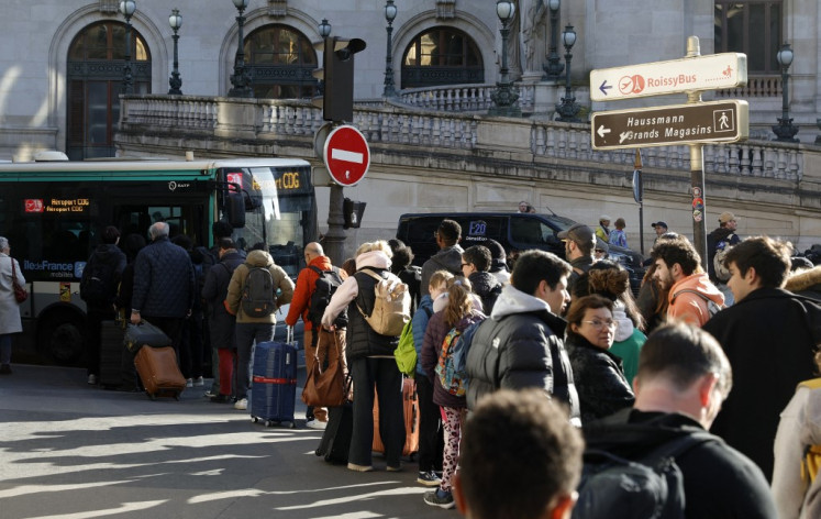 Passengers queue to take a bus from Opera district in order to reach Paris Charles-de-Gaulle Airport (CDG), as train traffic has been stopped at the Gare du Nord station in Paris on March 7, 2025, following the discovery of a World War II bomb. Railway services at the Gare du Nord station, that have been interrupted on March 7 morning after the discovery of a World War II bomb, will remain “highly disrupted throughout the day“, warned the Minister for Transport.