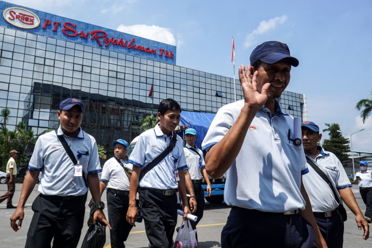 Workers wave to the camera on Feb. 28 as they leave a factory of textile giant PT Sri Rejeki Isman (Sritex) in Sukoharjo, Central Java. Sritex ceased operations on March 1 after being declared insolvent by the Semarang Commercial Court. 