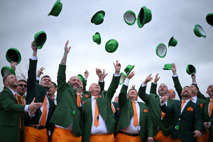 Racegoers dressed in the national colors of Ireland hurl their hats into the air during a Saint Patrick's Day celebration on March 13, 2025, the third day of the Cheltenham Festival at Cheltenham Racecourse in the western English town.