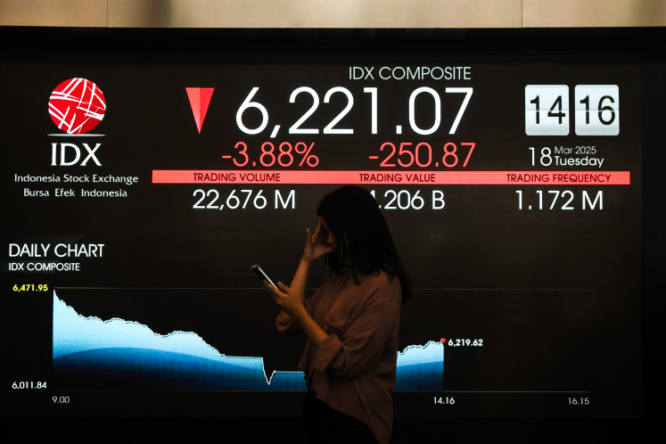 A woman walk beside stock prices at the Indonesia Stock Exchange in Jakarta on March 18, 2025.