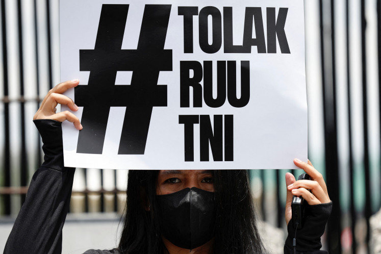 A woman holds a sign that reads, “Reject the TNI Bill,“ on March 20, 2025, during a protest against a revision to the military law, outside the House of Representatives building in Jakarta. 