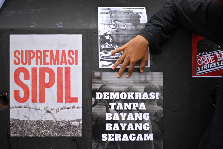 A protester puts up posters reading “Civilian supremacy“ (left) and “Democracy without uniformed shadows” (center, bottom) during a rally in Jakarta on March 20, 2025, to protest the passage of the revised Indonesian Military (TNI) Law.