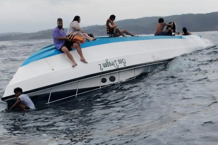 This handout from the Klungkung District Police taken on March 21, 2025 and released on March 22, 2025 shows survivors sitting on the hull of a capsized boat as they wait to be rescued after the snorkeling boat with tourists was hit by waves in Nusa Penida, Bali.
