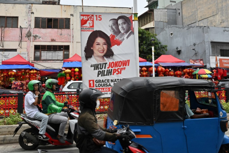 Jakarta motorists drive on Jan. 18, 2024, past a campaign banner for legislative candidate Grace Natalie Louisa from the Indonesian Solidarity Party (PSI) that also features party chair Kaesang Pangarep (right, top) and his father, then-president Joko “Jokowi“ Widodo.