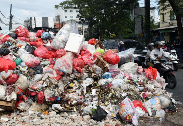 Motorists ride by a pile of trash on Wednesday in South Tangerang, Banten.