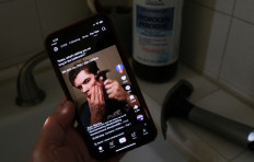 This illustration photo shows a video of male TikTok influencer hammering his cheekbone, playing on a smartphone in a bathroom next to a bottle of hydrogen peroxide and a hammer in Los Angeles, April 11, 2025. 