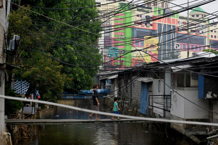 A man and a boy walk across a makeshift bridge on Nov. 26, 2019, beneath a web of electricity cables in a riverbank settlement in Jakarta.