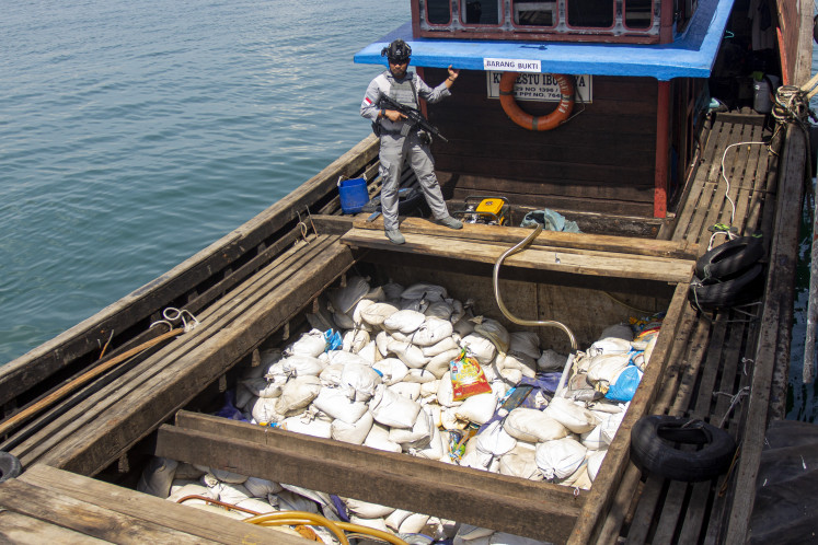An armed member of the Maritime Security Agency (Bakamla) guards 30 tonnes of illegal tin sand aboard the KM Doa Restu Ibu Jaya on April 28, 2025, after intercepting the smuggling attempt headed for Mersing in Johor Bahru, Malaysia.